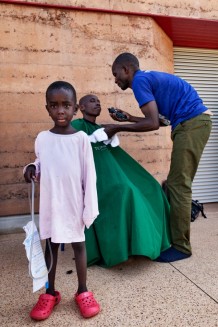 Children's Surgical Hospital. Family visit on Friday afternoon. Careb David Hakizimana, 5 years old, who underwent anoplasty for anorectal malformation, and the barber, who cuts a father's hair. Careb is from Burundi, he is one of the patients of the Regional Programme. Born with a congenital malformation, he was operated on in Burundi at 1 month, but the operation was not conclusive. Due to his illness he never went to school. Together with his mother, a farmer, he smiles big when he thinks that when he returns home he will be able to start studying. Entebbe, Uganda, 2023