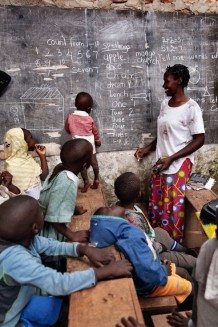 The kindergarten of the Katoogo slum school. Teacher Mbabazi Naume, 28, keeps her son Opio Messah, 1, in class. Kampala, Uganda, 2023